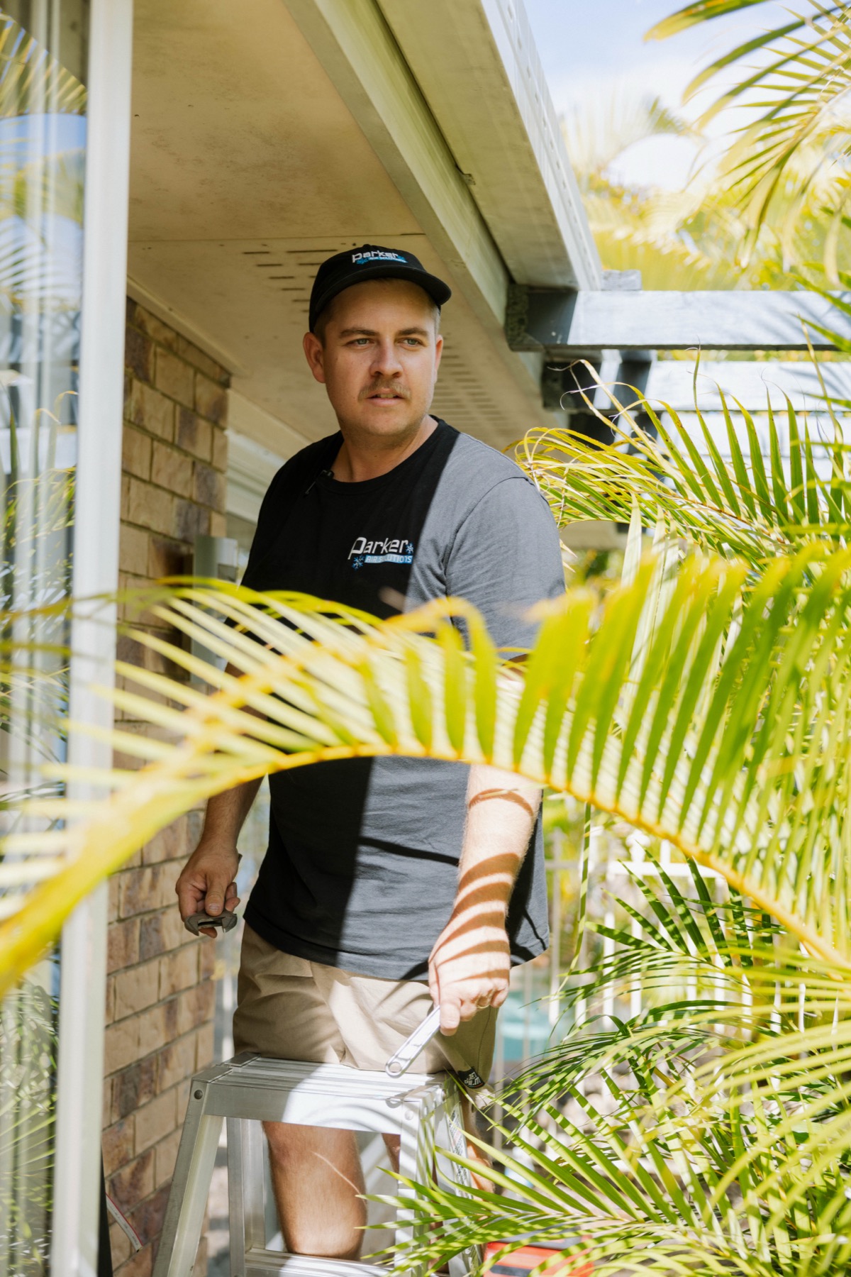 Parker Air technician working on exterior cable entry point among palm trees